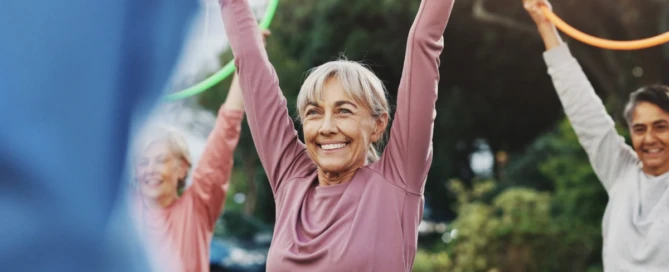 Older adults raise hula hoops during an outdoor fitness class, showing active independent living at La Conner Retirement Inn.