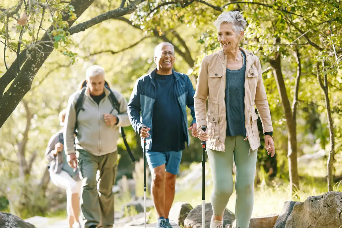 fitness over 65 - Older adult woman smiling while walking outdoors with walking poles